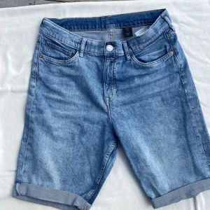 Blå jeansshorts med uppvik - Klassiska blå jeansshorts från H&M med fem fickor och snygga uppvikta benslut. Shortsen har normal passform och är tillverkade i mjukt denimtyg. Perfekta för varma dagar och enkel att matcha med t-shirt eller hoodie.