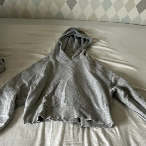 Grå croppad hoodie från Chiquelle - Säljer en grå croppad hoodie från Chiquelle i mjuk bomullsblandning. Tröjan har huva, långa ärmar och en relaxed fit med rå kant nertill. Perfekt för en chill och avslappnad stil.
