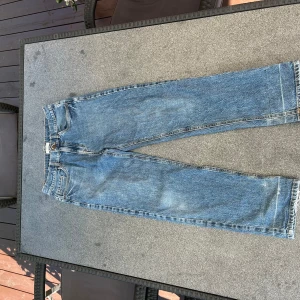 blå jeans straight fit -  jeans i blå denim med raka ben och femficksmodell. Jeansen har normal passform och knäppning fram. Snyggt slitna detaljer nertill på benen för en avslappnad vibe. Perfekta för dig som gillar tidlös stil.