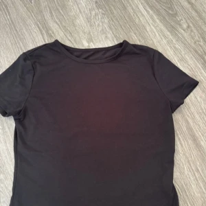 Svart basic t-shirt - Enkel svart t-shirt med rund hals och korta ärmar. Perfekt till jeans eller shorts och funkar året runt. T-shirten har en klassisk passform och är gjord i mjukt material som känns skönt mot huden.