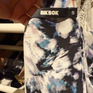 Mönstrad klänning med kedjeband BikBok - Säljer en cool kortklänning från BikBok med abstrakt svart, vit och blått mönster. Klänningen har smala axelband i guld-kedja och lång ärm. Perfekt för dig som vill sticka ut med en unik look!