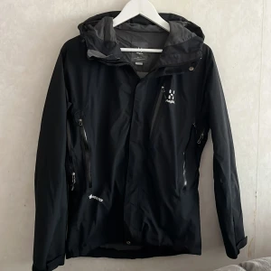 Svart vindjacka Haglöfs Gore-Tex S - Svart vindjacka från Haglöfs i storlek S, tillverkad i slitstark Gore-Tex. Jackan har flera dragkedjeförsedda fickor, justerbar huva och diskret logga på bröstet. Perfekt för dig som vill ha en stilren och funktionell jacka till vardagsäventyr. Nyskick, nypris 2900 (Pris kan diskuteras)