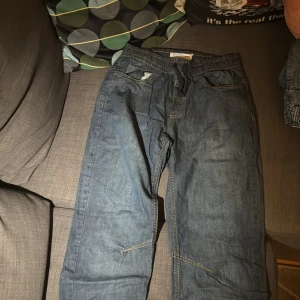 Blå jeansbyxor med snörning - Säljer ett par blå jeansbyxor med resår och snörning i midjan. Byxorna har raka ben och synliga sömmar, samt fickor fram. Perfekta för en avslappnad och chill stil.