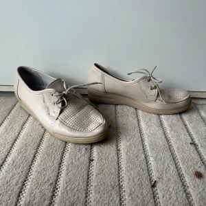 Beige skinnsneakers Lady Comfort 37 - Beiga sneakers från Lady Comfort i skinn med snörning och perforerade detaljer framtill. Skorna har platt sula och rund tå, perfekt för dig som gillar en enkel och clean stil. Klassisk modell som funkar till det mesta.