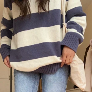 Randig stickad tröja Brandy Melville - Supermysig stickad tröja från Brandy Melville med breda mörkblå och vita ränder. Tröjan har rund hals, ribbade muddar och en oversized passform. Perfekt för kallare stunder. 