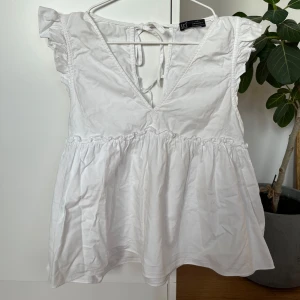 Vit blus med volangärm från Zara - Supersöt vit blus från Zara med volangärmar och v-ringning. Blusen har knytning i ryggen och en luftig, flowy passform med rynkade detaljer under bysten.
