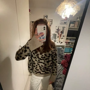 Beige leopardmönstrad stickad tröja - Snygg stickad tröja i beige med svart leopardmönster. Tröjan har rund halsringning, ribbade muddar och lång ärm. Perfekt för dig som vill sticka ut lite extra med ett djurmönster i garderoben. Den är i stl L men passar även mindre och större