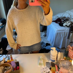 Vit stickad tröja med struktur - Supermysig vit stickad tröja med rund hals och lång ärm. Tröjan har en fluffig, strukturerad yta som ger en cool och avslappnad vibe. Perfekt att slänga på sig över ett linne eller t-shirt när det är lite kyligare ute.