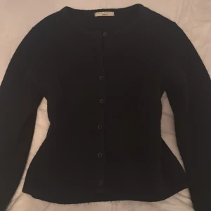 Svart kofta från Gina Tricot - En klassisk svart kofta från Gina Tricot i premiumkvalitet. Koftan har rund halsringning, långa ärmar och knäppning med svarta knappar framtill. Nästan helt ny använd få gånger och mjuk och len som när man köper den ny. Om du har frågor eller liknade skriv gärna💕
