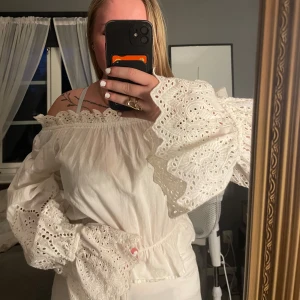 Vit offshoulder blus med broderade ärmar - Supersöt vit offshoulder blus med breda, broderade volangärmar och elastisk kant upptill. Blusen har romantiska spetsdetaljer och vackert hålmönster på ärmarna. 