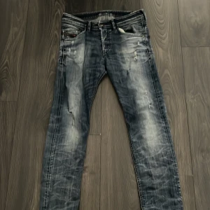 Disel jeans (byte) - Säljer ett par blå jeans med slitna detaljer. Jeansen har en tvättad look med ljusare partier och flera små revor för en trendig, använd känsla. Klassisk femficksmodell och dragkedjegylf.