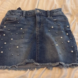 Jeanskjol med pärlor från Lindex - Snygg blå jeanskjol från Lindex med coola pärldetaljer framtill.