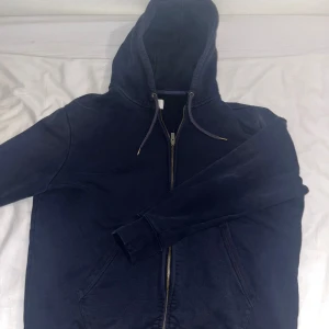 Mörkblå hoodie med dragkedja M&S - Mörkblå hoodie från M&S i storlek L. Tröjan har huva med snörning, hel dragkedja framtill och två fickor. Tillverkad i mjuk bomullsmix, perfekt för chill dagar. Klassisk och enkel design som funkar till det mesta.