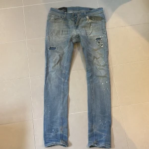 Dondup jeans  - Säljer ett par blå skinny jeans från dondup i storlek 31. Jeansen har slitna detaljer, hål på låren och stänk som ger en cool, använd look. Klassisk femficksmodell med dragkedja och knapp. Perfekta för dig som gillar streetstyle. Modellen är George. Finns fler jeans på profilen.