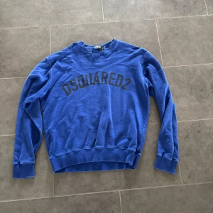 Blå sweatshirt från Dsquared2 - Blå sweatshirt från Dsquared2 med svart logotyptryck över bröstet. Tröjan har rund halsringning, långa ärmar och ribbade muddar vid ärmslut och nederkant. Perfekt för en avslappnad och cool stil.