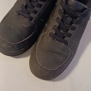 Svarta sneakers Court SNK JR - Svarta sneakers från Spine. Skorna har klassisk design med rund tå, svarta snören och platt sula. Perfekta för dig som gillar en clean och enkel stil. Tillverkade i syntetmaterial.