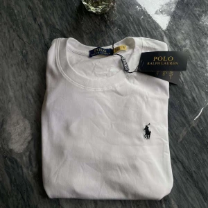 Vit t-shirt från Polo Ralph Lauren - Klassisk vit t-shirt från Polo Ralph Lauren med rund hals och korta ärmar. T-shirten har den ikoniska broderade loggan i svart på bröstet och är gjord i mjuk bomull. Perfekt basic-plagg med snygg passform och stilren look.