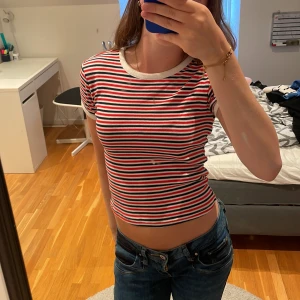 Randig croppad topp från H&M Divided - Säljer en croppad topp från H&M Divided i storlek XS. T-shirten har röda, vita och marinblå ränder, rund halsringning och korta ärmar med vita kanter. Perfekt för dig som gillar en färgglad och avslappnad stil. Köparen står för frakten 