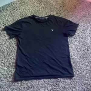 Svart t-shirt från Gant med brodyr - Aldrig använd.Svart t-shirt från Gant med klassisk passform och liten broderad Gant-logga på bröstet. T-shirten har rund halsringning och är tillverkad i mjuk bomull. Perfekt för en clean och stilren look.