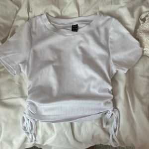 Vit ribbad topp med snörning - Vit ribbad topp med korta ärmar och snygg snörning i sidorna. Croppad modell. Knappt använd! Pris går att diskutera😊