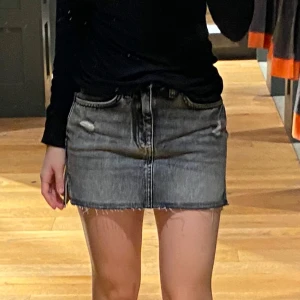 Grå jeanskjol från Superdry, strl 26 - Säljer en grå, tvättad jeanskjol från Superdry med slitna detaljer och rå kant nertill. Kjolen har klassisk femficksmodell, dragkedja och knapp framtill. I ett väldigt bra skick.