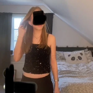 Svart paljettlinne  - Säljer ett svart linne täckt av glittriga paljetter, perfekt för dig som vill sticka ut. Modellen är en  croppad  tubtopp och har en rak passform. Ger en riktigt snygg partyvibe och passar till både jeans och kjol.