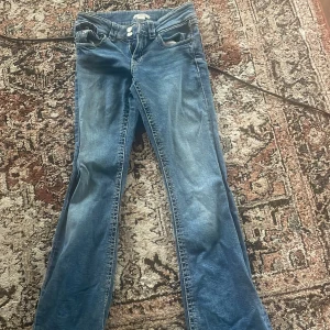 Blå bootcut jeans från Gina Tricot - Snygga blå jeans från Gina Tricot med bootcut-modell och klassisk femficksdesign. Jeansen har dubbla knappar i midjan och är tillverkade i mjukt denimtyg. Perfekta för dig som gillar jeans med utsvängda ben.