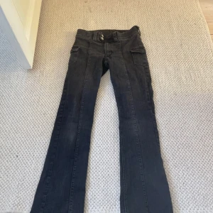 Svarta bootcut jeans från H&M - Snygga svarta bootcut jeans från H&M med låg midja och justerbar linning. Jeansen har coola fickor på sidorna och dubbla knappar i midjan. Perfekta för dig som gillar en klassisk men trendig look. Använd 2-3 ggr och priser kan diskuteras!💕