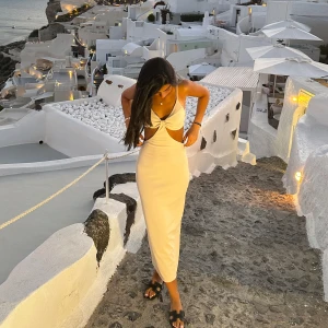 Champagnefärgad långklänning med cut-outs - Supersnygg långklänning i champagnefärg med smala axelband och trendiga cut-outs vid midjan. Klänningen har en twistad detalj framtill och figurnära passform som framhäver siluetten. Perfekt för varma sommarkvällar och semester vibes.