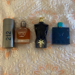 Fyra herrparfymer från kända märken - Säljer fyra snygga herrparfymer: 212 i silverfärgad cylinder, Stronger With You Intensely i fyrkantig glasflaska med bärnstensfärgad vätska, Le Male i mörkblå kroppformad flaska med gulddetalj och Versace Eros i blå kvadratisk flaska med turkos kork.