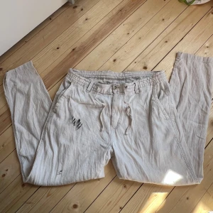 Beiga linnebyxor med snörning - Snygga beiga linnebyxor med avslappnad passform och snörning i midjan. Byxorna har sidofickor, bälteshällor och raka ben. Perfekta för varmare dagar och ger en chill vibe till din outfit.