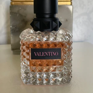 Valentino Eau de Parfum 50ml - Lyxig parfym från Valentino i en cool, fyrkantig glasflaska med nitar och mönstrad yta. Flaskan är transparent med ljusrosa doftvätska och svart etikett med rosa text. Rymmer 50 ml Eau de Parfum och har en snygg svart kork med pyramidnitar.