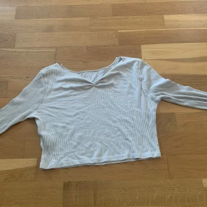Ljusribbad croppad långärmad topp - Säljer en ljus, ribbad och croppad långärmad topp med v-ringning. Perfekt för dig som gillar en enkel men ändå snygg stil. Tunt och mjukt material som känns skönt mot huden. Passar till både jeans och kjol för en chill look.