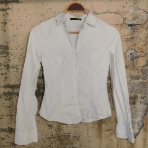 Vit figursydd skjorta från Brandy Melville - Snygg vit skjorta med klassisk krage och långa ärmar. Skjortan har figurnära passform och knäppning framtill. Perfekt till jeans eller kostymbyxor för en clean och stilren look.