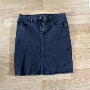 Svart jeanskjol från Pieces XS - Svart jeanskjol från Pieces i klassisk fyrficksmodell. Kjolen är kort och har rå kant nertill för en cool, avslappnad vibe. Passar perfekt till sneakers eller boots och har dragkedja och knapp framtill.