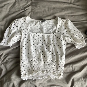 Prickig blus från Gina Tricot XS - Supersöt vit blus med svarta prickar från Gina Tricot. Modellen har fyrkantig ringning, puffiga korta ärmar med resår och smockad nederdel med volangkant🥰