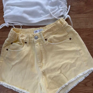 Gula jeansshorts från Zara - Snygga ljusgula jeansshorts från Zara med råa fransade kanter och klassisk femficksmodell. Shortsen har hög midja och är perfekta för sommardagar. De är gjorda i mjuk bomull och har knapp och dragkedja framtill.