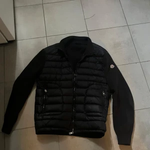 Moncler cardigan. - Snygg mörkblå cardigan från Moncler med quiltad front och ärmar i stickad bomull. Jackan har dragkedja framtill, två fickor med dragkedja och Moncler-logga på ena ärmen. Perfekt för dig som vill ha en stilren och exklusiv look. Storlek xl men passar M/L.