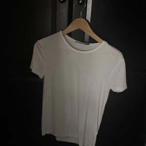 Vit basic t-shirt från 157 - En klassisk vit t-shirt från 157 i storlek S. T-shirten har rund halsringning och korta ärmar, perfekt för en clean och enkel look. Tillverkad i mjukt material som känns skönt mot huden. Passar till allt och är ett måste i garderoben.