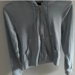 Ljusgrå hoodie med dragkedja - Snygg ljusgrå hoodie med dragkedja framtill och två stora fickor. Tröjan har huva med snörning och långa ärmar. Perfekt för en avslappnad stil och enkel att matcha med jeans eller mjukisbyxor.