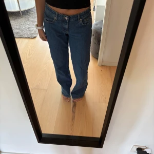 Blå raka jeans - Säljer ett par klassiska blå jeans med rak passform och låg midja. Jeansen är i bra skick förutom lite slitna längs ner