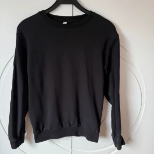 Svart Moschino sweatshirt med logoband - Svart sweatshirt från Moschino med långa ärmar och breda logoband längs båda ärmarna. Bandet är vitt med svart text och en röd linje. Tröjan har rund halsringning och ribbade muddar. Perfekt för dig som gillar streetstyle och vill sticka ut. Priset kan diskuteras vid en snabb affär