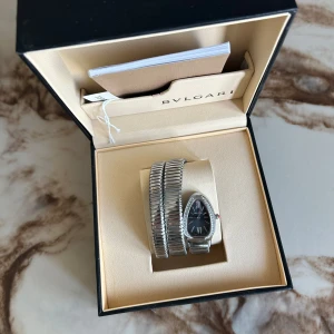 Bulgari Serpenti dam klocka - Exklusiv Bvlgari Serpenti klocka med svart urtavla och silverfärgat, spiralformat armband. Klockan har en droppformad boett med gnistrande stenar runt urtavlan och klassiska romerska siffror. Säljs i originalask med tillhörande dokumentation. Ny pris är runt 80 000 kr!!