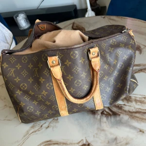 Louis Vuitton monogram handväska - Säljer en klassisk brun handväska från Louis Vuitton med ikoniskt monogrammönster och detaljer i ljust skinn. Väskan har två handtag, dragkedja upptill och rymligt innerfack. Perfekt för dig som vill ha en tidlös och lyxig accessoar.