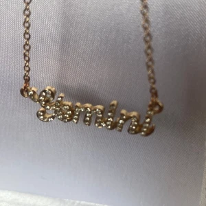 Guldigt halsband med Gemini-text -  halsband i guld med kedja och ett hängsmycke där det står 'Gemini' i glittriga stenar. Perfekt för dig som vill visa ditt stjärntecken med stil. 