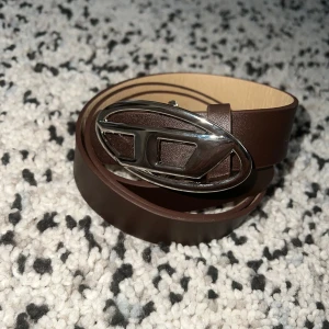 Vintage Diesel Belt  - Snyggt brunt bälte i skinn med ett ovalt, silverfärgat spänne som har en unik design. Perfekt accessoar för att lyfta din outfit med en stilren touch. Bältet har en klassisk form och passar till många olika looks.