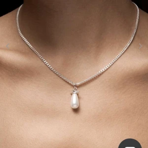 Maria Nilsdotter halsband med pärlhänge - Stilrent halsband från Maria Nilsdotter med en kedja i silver och ett droppformat vitt pärlhänge. Hänget har en unik detalj upptill som ger smycket en cool och modern känsla. Perfekt för dig som gillar minimalistiska men ändå iögonfallande accessoarer. Kedjan är 50cm