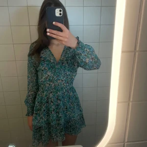 Blommig klänning Zara - Supersöt kortklänning i blått/grönt med blommigt mönster och volangkant. Klänningen har v-ringning, långa ärmar med resår vid handlederna och markerad midja. Perfekt för sommaren och nu till midsommar💞💞