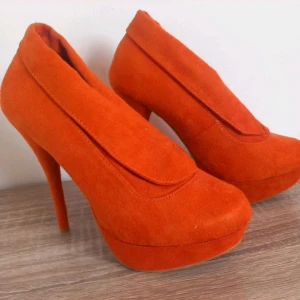 Orange mocka pumps med platå och klack - Snygga pumps i starkt orange mocka med hög klack och platåsula. Skorna har en rund tå och en stilren design utan synliga detaljer. Perfekta för dig som vill sticka ut med färg och höjd.