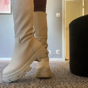 Beiga höga boots med chunky sula - Snygga höga boots från Steve Madden i beige med grov, chunky sula och dragkedja på insidan. Skorna är tillverkade i ett syntetmaterial med lätt textur och har en rund tå.  Använda  2 gånger, nästans som nya. OBS liten missfärgning på inner sula (se sista bild). (Nypris: 2300kr)